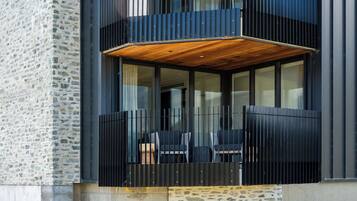 A modern building with a stone facade, a balcony with wooden flooring, and black-framed glass windows.