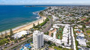 Eine Küstenstadt mit Strand, Hochhäusern und einem markanten Hotel mit Pool.