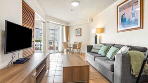 Ein Wohnzimmer mit einem Flachbildfernseher, einem grauen Sofa mit Kissen, einem Holztisch und einem Essbereich mit Stühlen und Tisch.