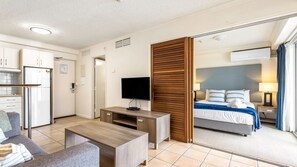 A hotel room with a bed, a TV, a desk, a sofa, and a mirror. - Sun & Surf Pad Resort Living, Alexandra Headland (Alexandra Headland)