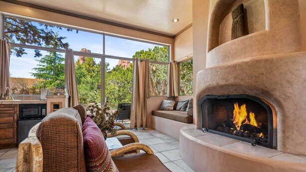 A cozy living room with a fireplace, large windows, and a stone wall. - Sunset- Sedona Villas (Sedona)