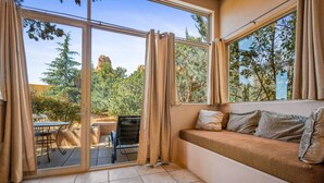 A room with a large sliding glass door leading to an outdoor patio, a cushioned bench with pillows, and a small table. - Sunset- Sedona Villas (Sedona)