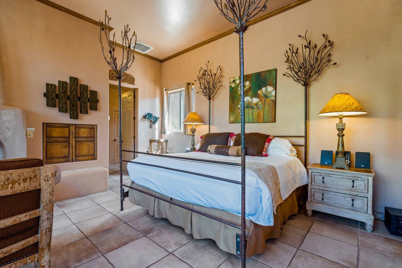 Une chambre à coucher avec un lit à baldaquin, une table de chevet avec une lampe, une commode et des œuvres d’art murales.