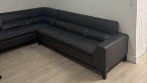 A room with a black sectional sofa, a white door, and a ceiling light fixture. - 3BR house+loft near Wynwood, perfec getaway! (Miami)