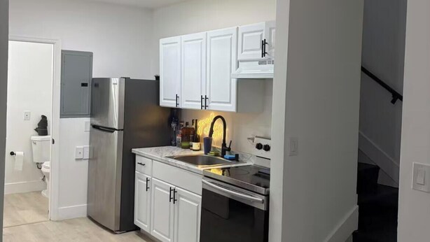 A modern kitchen with white cabinets, stainless steel appliances, and a black staircase. - 3BR house+loft near Wynwood, perfec getaway! (Miami)