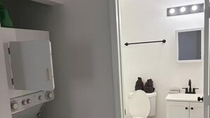 A compact bathroom with a washing machine, toilet, sink, and a mirror. - 3BR house+loft near Wynwood, perfec getaway! (Miami)