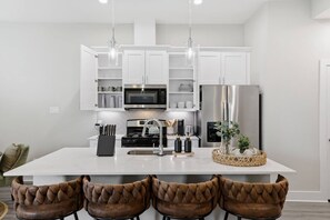 A modern kitchen with white cabinetry, stainless steel appliances, and a central island with bar stools. - Unwind 15 Min from Dwntn Houston in Tranquility! (Houston)