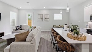 A modern kitchen with a central island, bar stools, and a dining area with a sofa and chairs. - Unwind 15 Min from Dwntn Houston in Tranquility! (Houston)