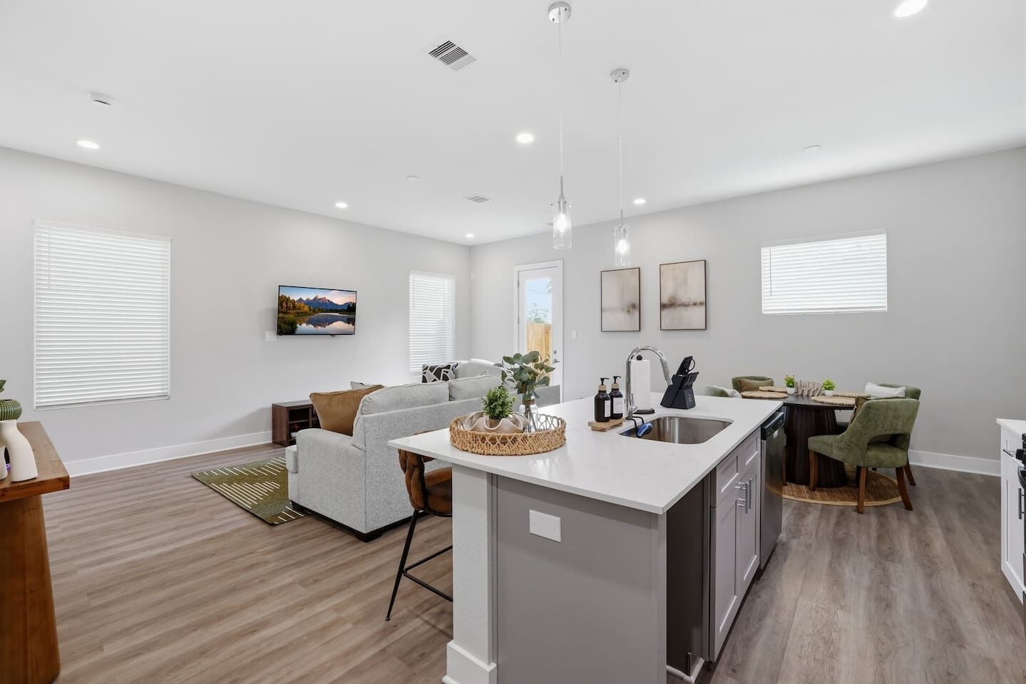 A modern kitchen with a central island, a dining area with chairs, and a living room with a sofa.