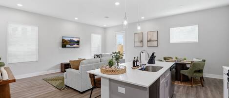 A modern kitchen with a central island, a dining area with chairs, and a living room with a sofa.