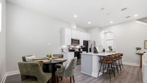 A modern kitchen with white cabinetry, a central island with stools, and a dining area with a round table and chairs. - Unwind 15 Min from Dwntn Houston in Tranquility! (Houston)