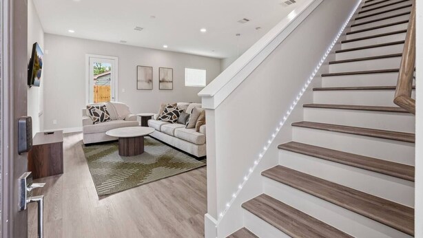 A modern living room with a staircase, wooden flooring, and a view of the outdoors. - Unwind 15 Min from Dwntn Houston in Tranquility! (Houston)