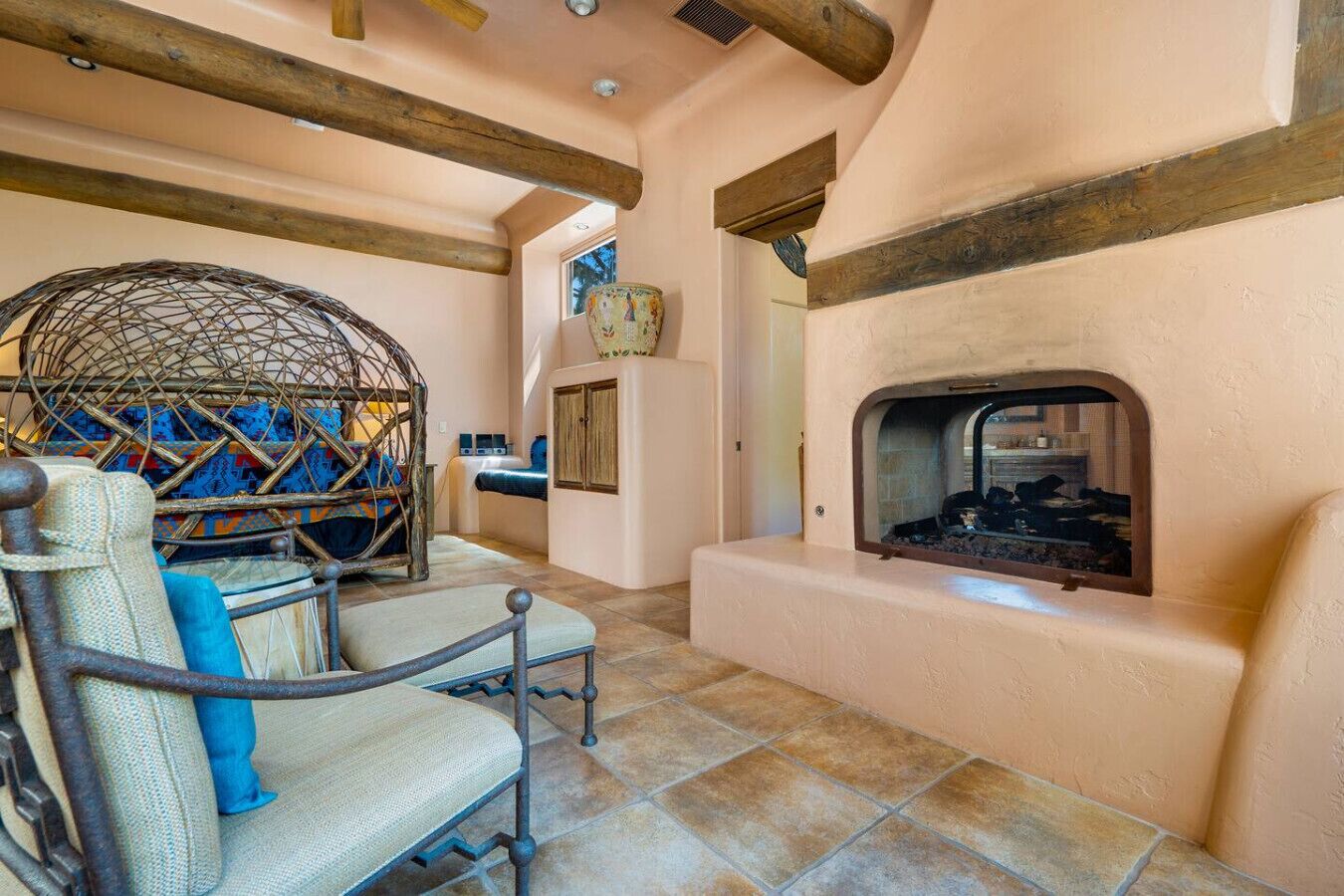 A cozy room with a fireplace, a woven chair, and a rustic ceiling.