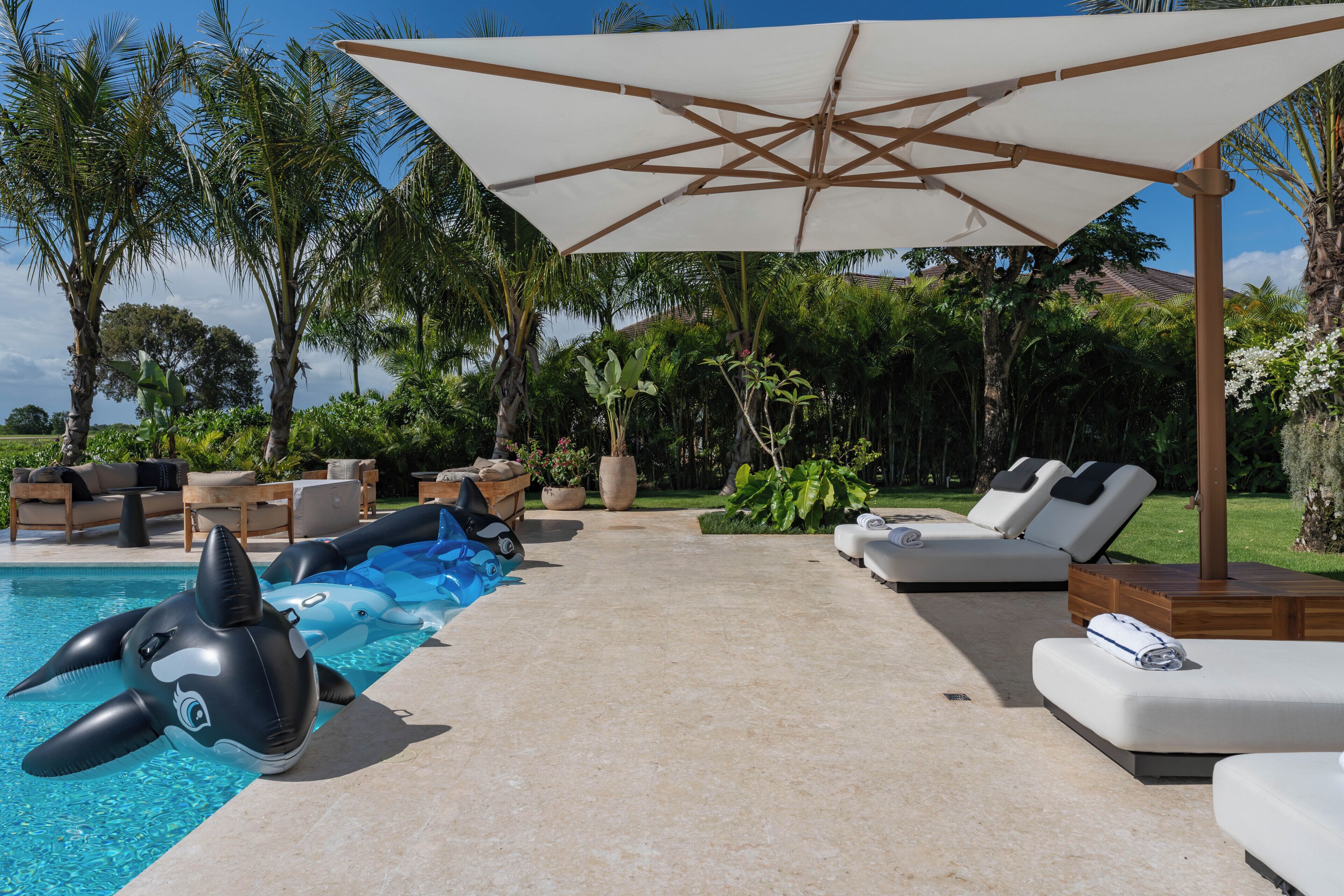 Un espace aménagé au bord de la piscine, avec des chaises longues, un requin gonflable et un grand parasol.
