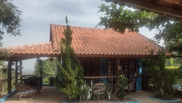 A building with a tiled roof, a covered patio area, and a garden with various plants. - chale sao francisco (São Pedro)