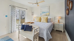 Quarto com cama, mesas de cabeceira, ventilador de teto e vista para o exterior.