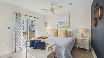A bedroom with a bed, bedside tables, a ceiling fan, and a view of the outside.