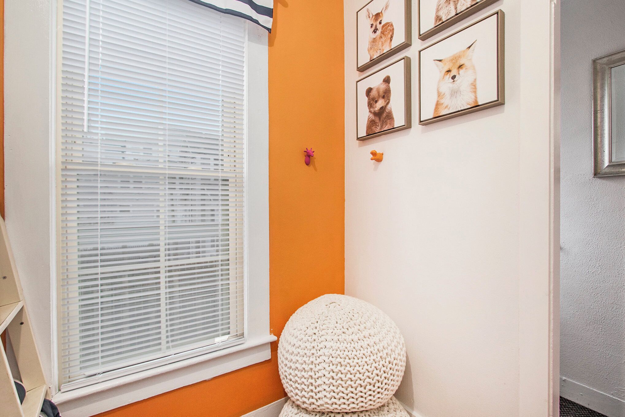 Een kamer met een raam, een rond geweven zitkussen en afbeeldingen van dieren in lijsten aan de muur.