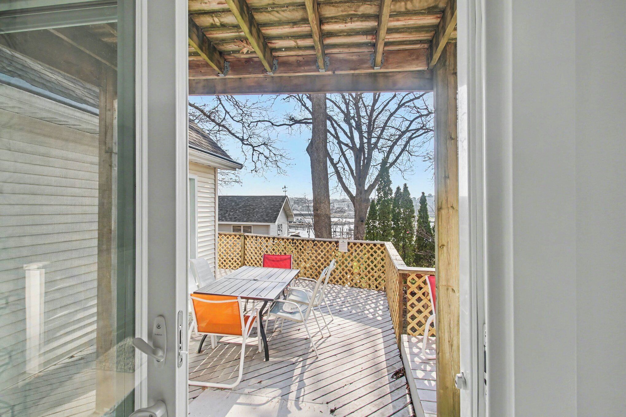 A deck with a table and chairs, a wooden fence, and a view of a house and trees.