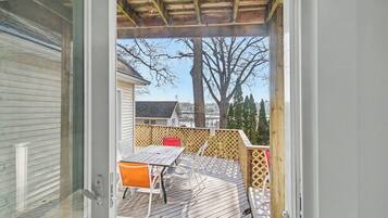A deck with a table and chairs, a wooden fence, and a view of a house and trees.