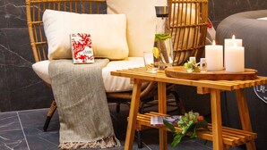 A wicker chair with cushions, a small table with candles, a bottle, and a decorative item. - Casino 2 - Sauna Whirlpool Game-zone (Hoehr-Grenzhausen)