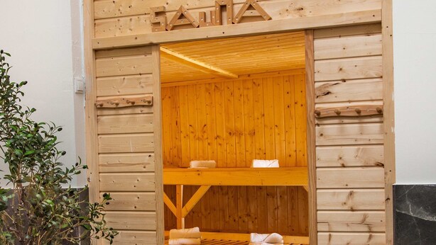 A wooden sauna entrance with a bench inside, a small table with candles, and a potted plant outside. - Casino 2 - Sauna Whirlpool Game-zone (Hoehr-Grenzhausen)
