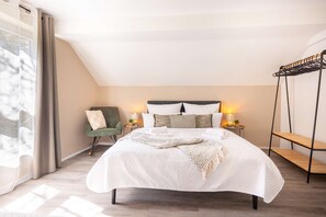 Un dormitorio con una cama grande, una silla, mesitas de noche y un estante colgante.