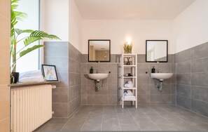 A bathroom with two sinks, a radiator, a shelf with towels, and a potted plant. - Villa Rheinsteig Sauna-whirlpool-kino (Bendorf)