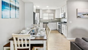 Una cucina moderna con mobili bianchi, un tavolo da pranzo apparecchiato e un divano grigio nella zona living.