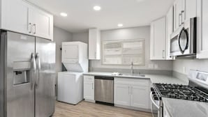 Una cucina moderna con elettrodomestici in acciaio inossidabile, mobili bianchi e pavimento in legno.