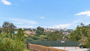Vista di un paesaggio urbano con una recinzione verde, una passerella in legno e un'auto parcheggiata.