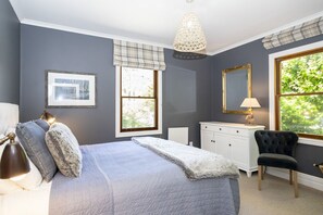Une chambre à coucher comprenant un lit, une lampe de chevet, une commode, une chaise et une fenêtre donnant sur un paysage verdoyant.