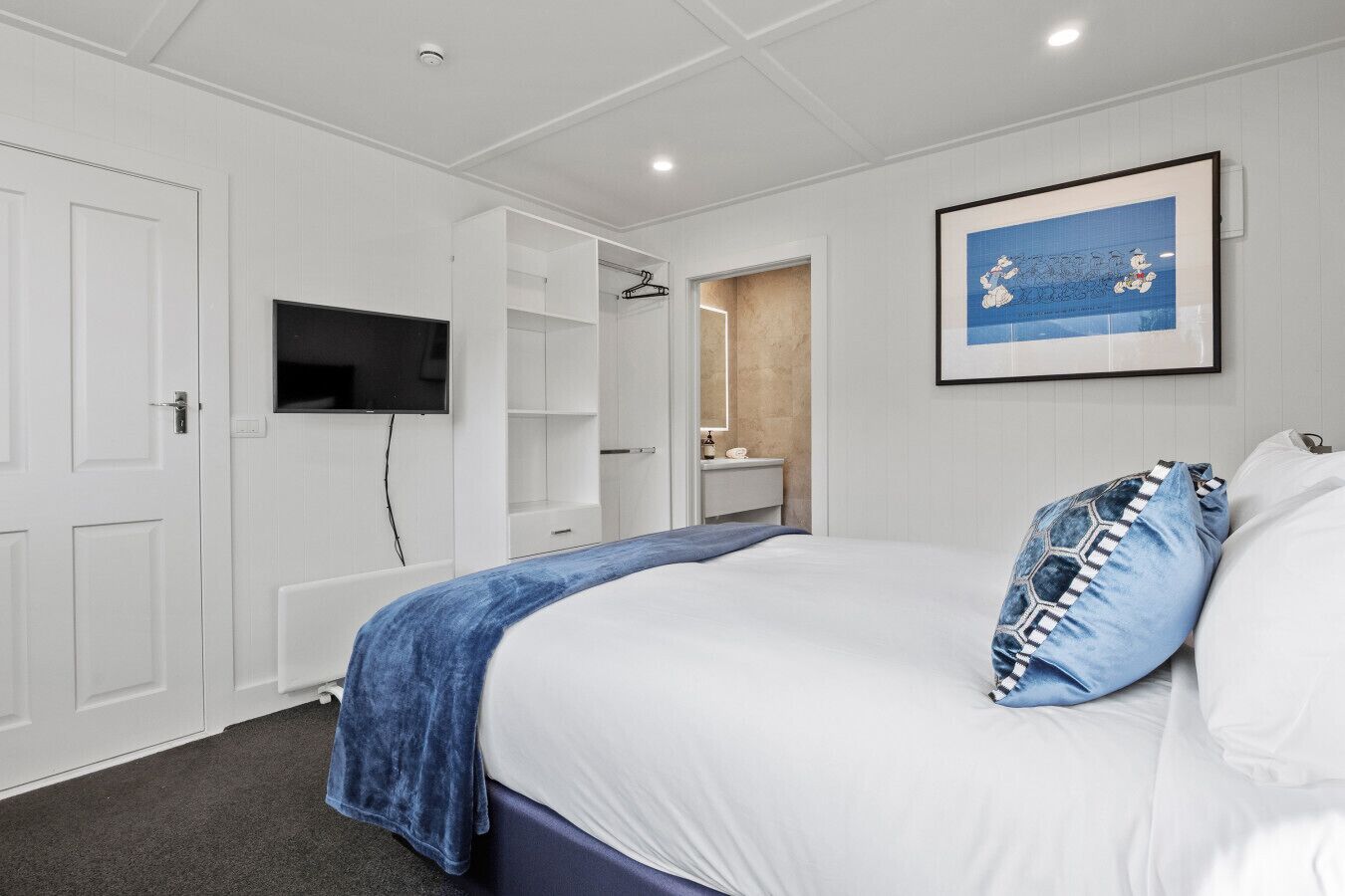 A bedroom with a bed, a TV, a wardrobe, and a bathroom visible through an open door.