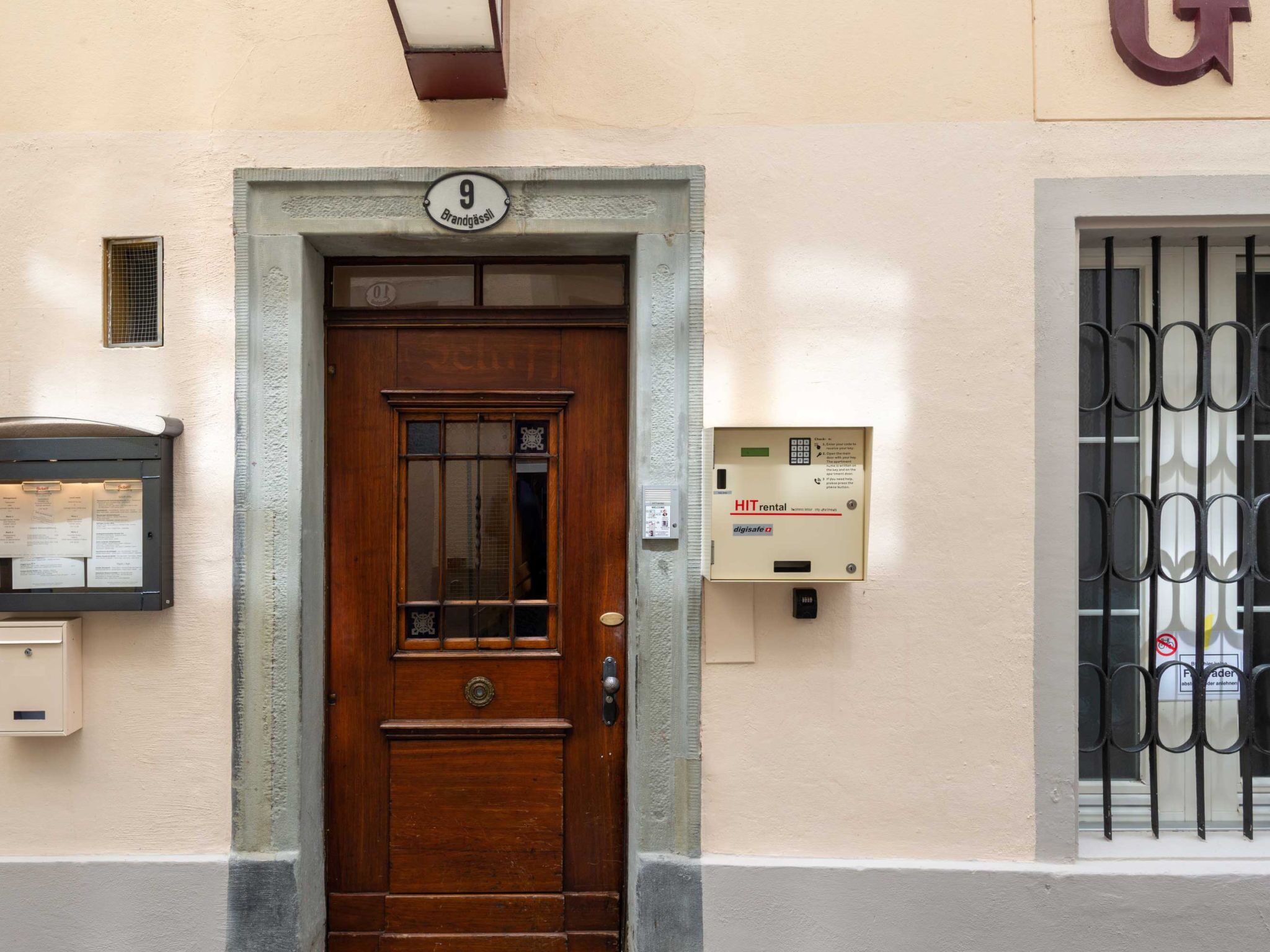 Una puerta de madera con un cartel con número, un buzón y un buzón de seguridad en la pared.