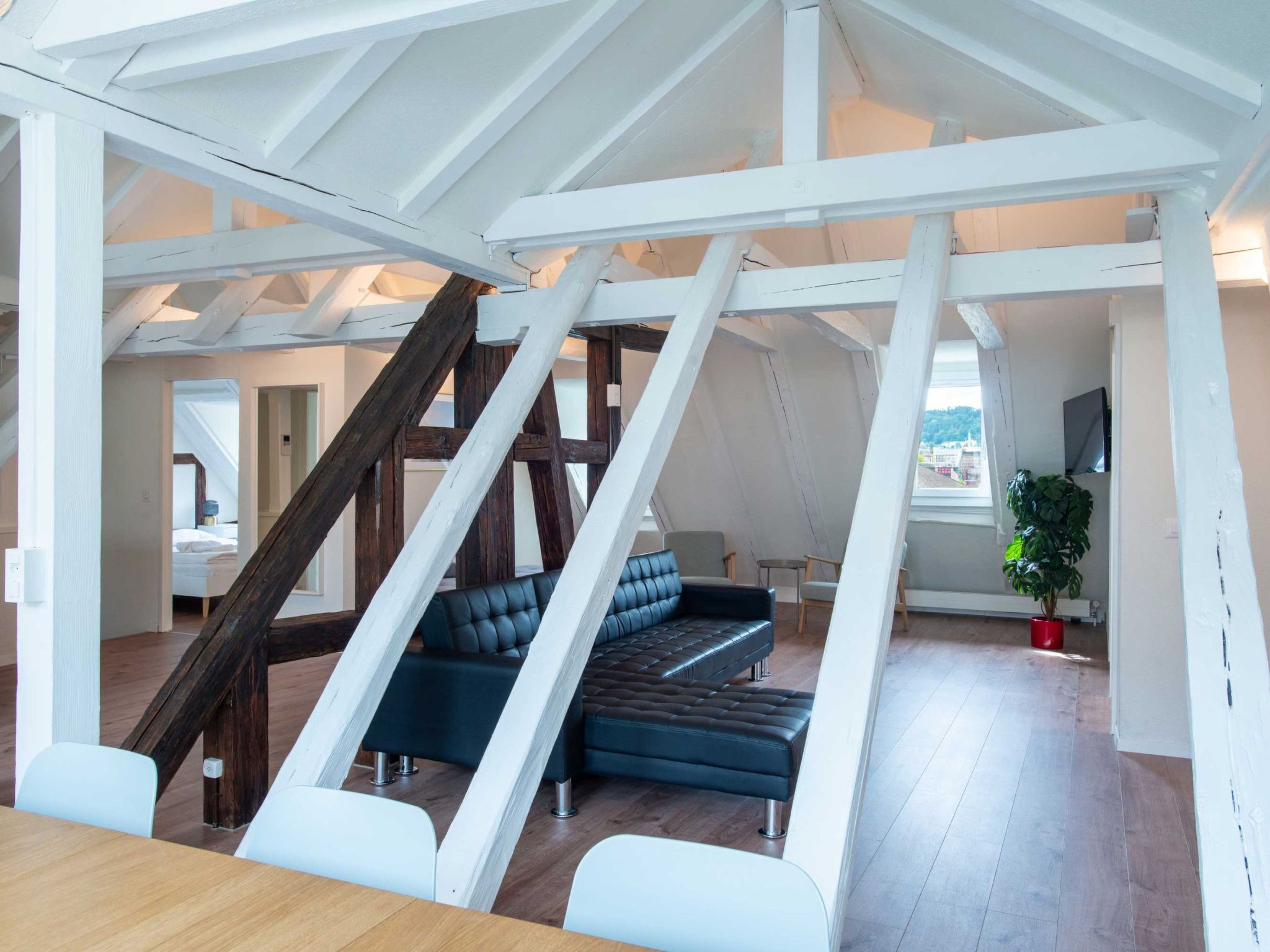 A spacious loft with exposed wooden beams, a dark blue sofa, and a dining area with a wooden table and chairs.