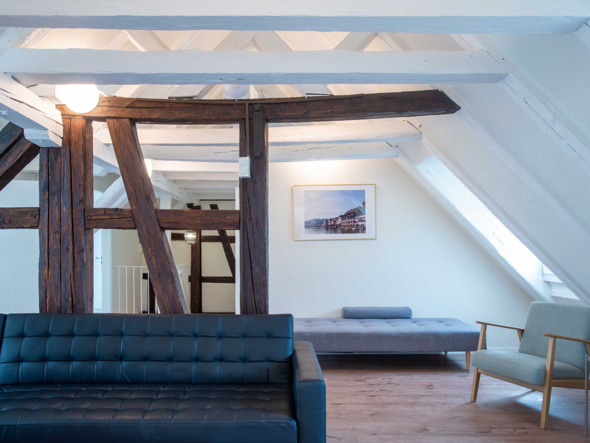 Ein Loft-Zimmer mit freiliegenden Holzbalken, einem blauen Sofa, einer grauen Bank und einem gerahmten Bild an der Wand.