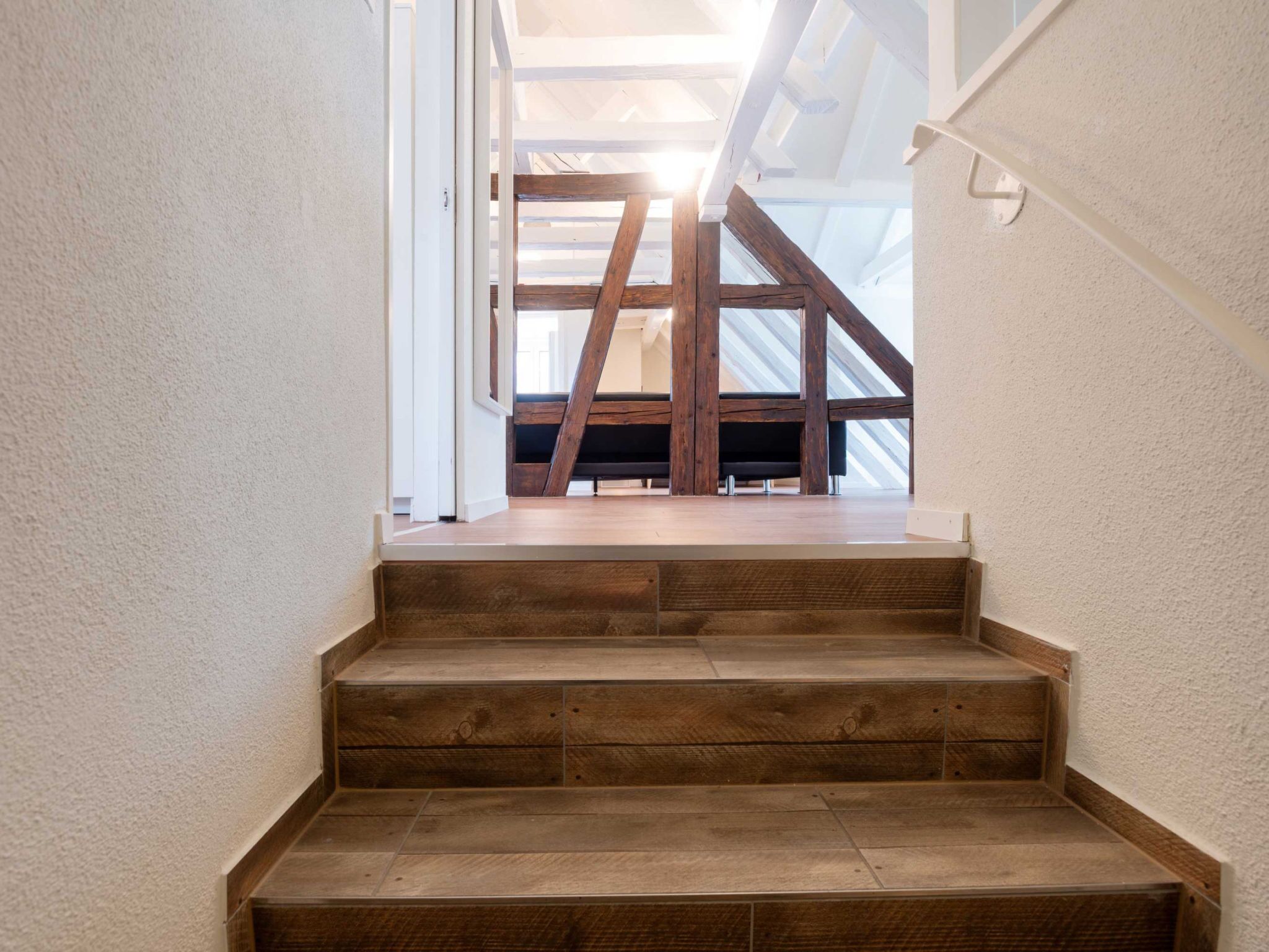 Una escalera de madera que conduce a un piso superior con vista al cielo a través de un tragaluz.