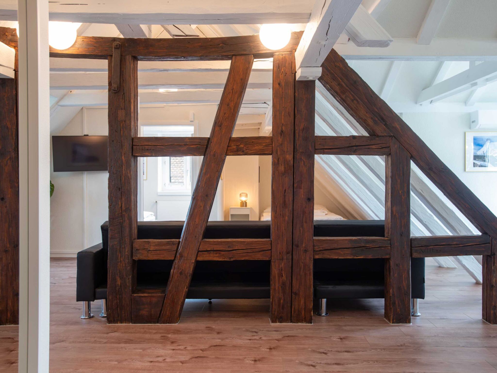 Um quarto estilo loft com vigas de madeira aparentes, um sofá preto e um claraboia.