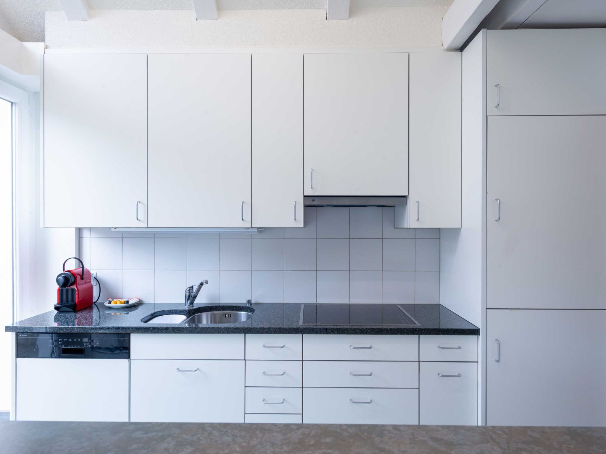 Una cocina moderna con armarios blancos, encimera negra y pileta de acero inoxidable.
