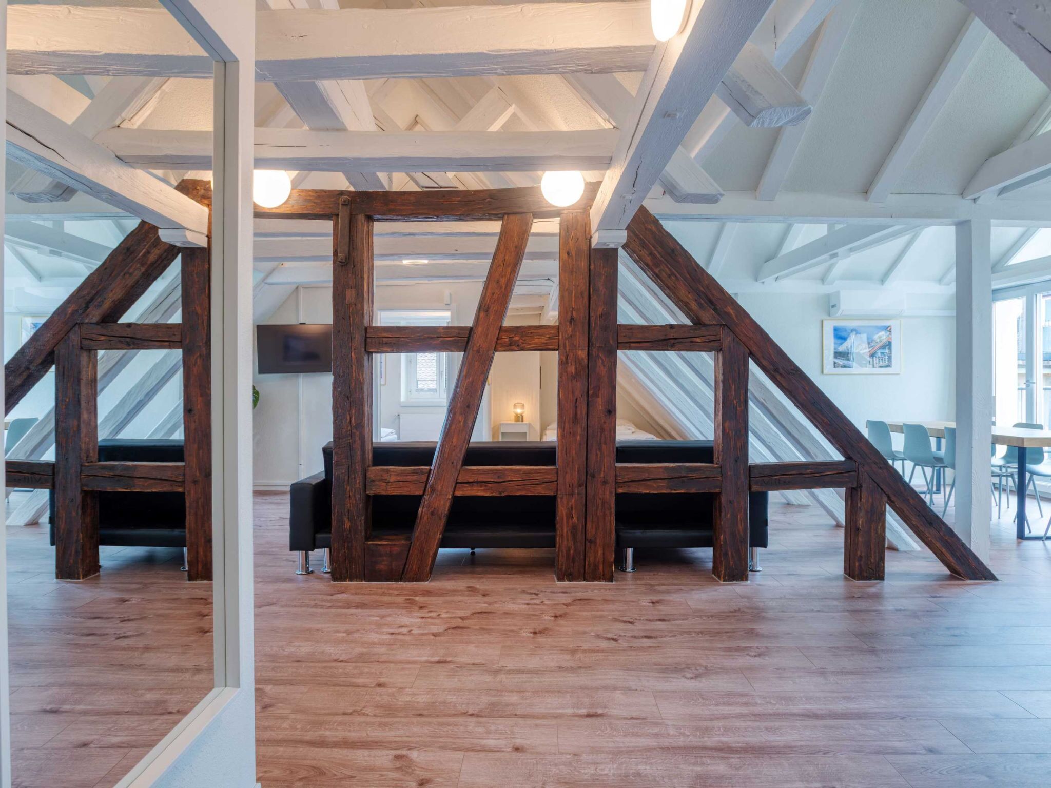 Un amplio ático con vigas de madera a la vista, un ventanal grande y un sofá moderno.