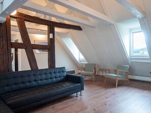 Ein Loft-Zimmer mit einem dunkelbraunen Ledersofa, zwei hellen Sesseln und einer Holzbalkendecke.