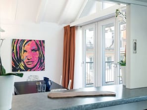 Eine moderne Küche mit Essbereich, einem großen Fenster mit Vorhängen und einem farbenfrohen Gemälde an der Wand.