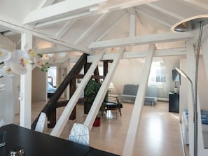 Ein geräumiges Loft mit hohen Decken, freiliegenden Holzbalken, einer Treppe und einer modernen Sitzecke.