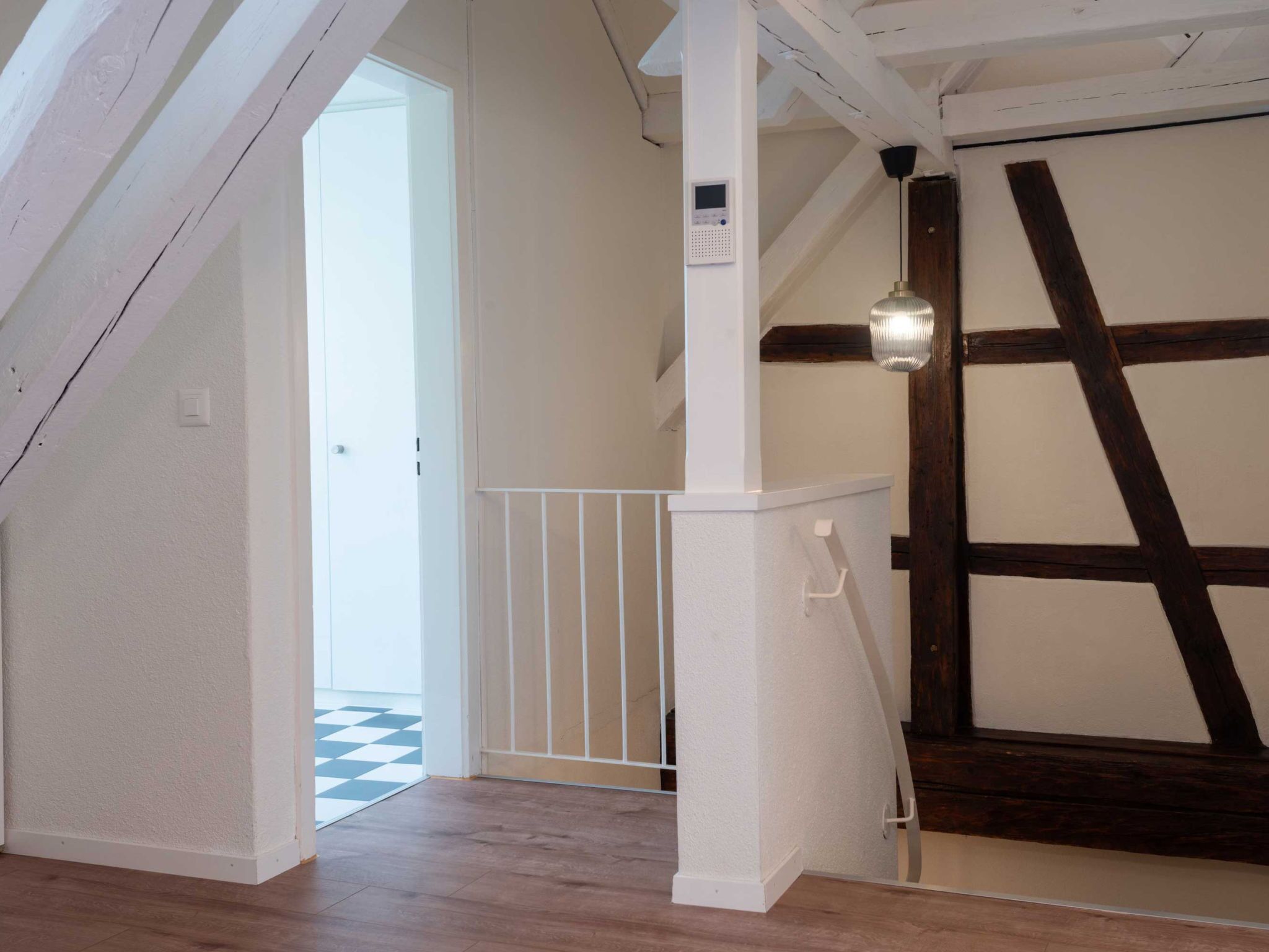 Un pasillo con piso de madera, baranda blanca y una puerta que da a otra habitación.