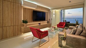 Ein modernes Wohnzimmer mit Flachbildfernseher, roten und grauen Sofas, einem Glastisch und Blick auf die Stadt.