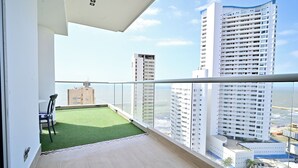 Ein Balkon mit Blick auf hohe Gebäude, eine kleine Rasenfläche und ein Stuhl.