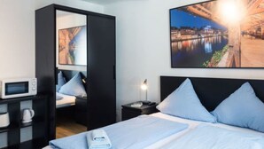 Ett hotellrum med en säng, ett nattduksbord, en mikrovågsugn, en garderob och en stor målning som föreställer en stadsbild.