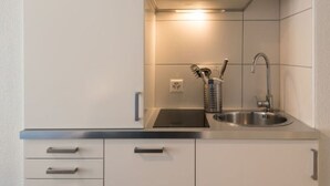 Ett modernt kök med en diskho i rostfritt stål, en köksfläkt och ett förvaringsställ för köksredskap.
