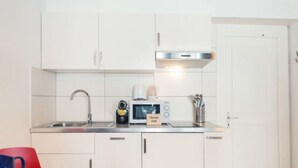 Una cucina compatta con mobili bianchi, un lavello in acciaio inossidabile, un forno a microonde e un tostapane.