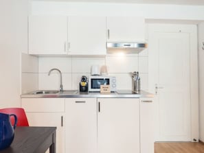 Eine kleine Küche mit weißen Schränken, einer Edelstahl-Spüle, einer Mikrowelle und einem Toaster.